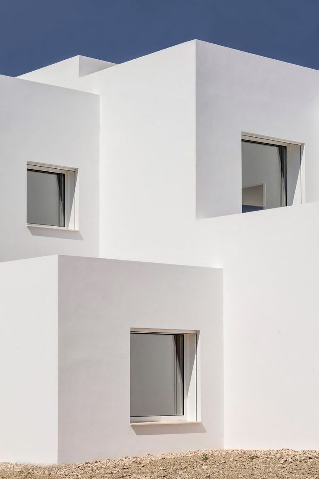 Volúmenes blancos escalonados con ventanas profundas bajo un cielo despejado.